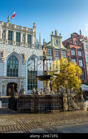 DANZIG, POLEN - 08. Okt 2021: Neptuns-Brunnen vor dem Artus-Hof-Gebäude mit Stadtflagge auf der Oberseite in Danzig, Polen Stockfoto