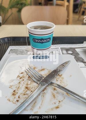 Sankt Petersburg, Russland - 21. Juni 2021. Eine Einweg-Tasse mit Tee und dem Cinnabon-Kuchen begann und endete, Gabel und Messer, auf dem Tisch Stockfoto