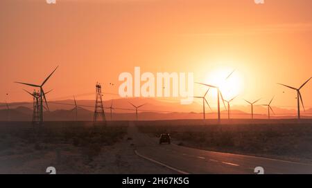 Auto, das mit Windmühlen und Strommasten in den Sonnenuntergang fährt Stockfoto