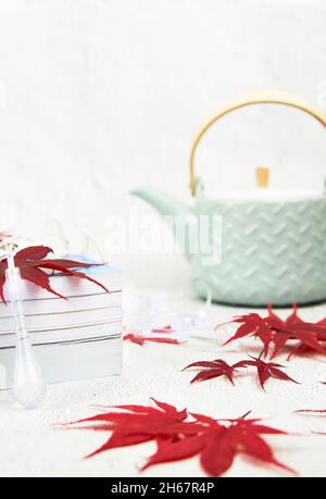 Hellgrüne Teekocher mit roten Ahornblättern und Büchern auf weißem Hintergrund. Textbereich. Stockfoto