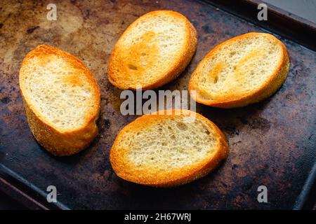 Geröstete Scheiben französisches Brot auf einem Blech Pfanne: In Scheiben geschnittenes Baguette, beträufelt mit nativem Olivenöl extra und geröstet auf einem Keksblatt Stockfoto