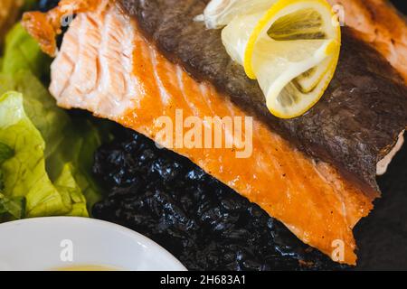 Geröstetes Lachsfilet auf schwarzem Teller mit Zitrone und Salat Draufsicht Stockfoto