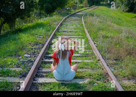 Ein Tourist in einem Hut sitzt mit dem Rücken auf der Eisenbahn Stockfoto