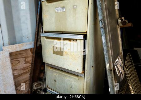 Ein alter Aktenschrank mit halb geöffneter Schublade, umgeben von Müll, der in einem Behälter gelagert wurde Stockfoto