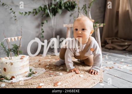 Hübsches Baby im ersten Jahr Geburtstag, Kleinkind mit Kuchen auf dem Boden, rustikale Dekoration. Stockfoto