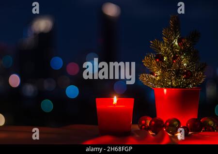 Brennende Kerze im roten Glas mit Weihnachtsbaum und Kugel Ornamenten auf bunten Stadt Bokeh Licht Hintergrund. Stockfoto