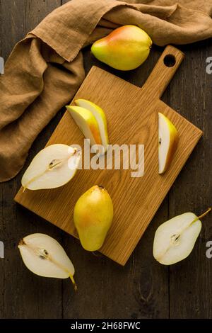 Geschnittene grüne Birnen auf Holzschneidebrett. Lebensmittel Hintergrund vertikal. Gesunder vegetarischer Snack. Küchengeräte Leinen Serviette Oberfläche. Fruchtzubereitung ein Stockfoto