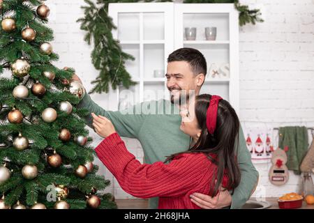 Glückliches Ehepaar schmückt am Vorabend von Weihnachten einen Weihnachtsbaum. Stockfoto