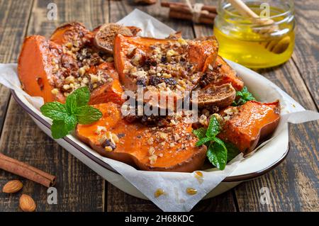 Gebackene Kürbisscheiben mit Nüssen, Honig und getrockneten Früchten auf einem hölzernen Hintergrund. Nahaufnahme. Richtige Ernährung, diätetische Mahlzeit. Nährwert von Gemüse Stockfoto
