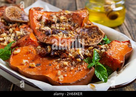 Gebackene Kürbisscheiben mit Nüssen, Honig und getrockneten Früchten auf einem hölzernen Hintergrund. Nahaufnahme. Richtige Ernährung, diätetische Mahlzeit. Nährwert von Gemüse Stockfoto