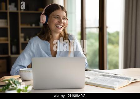 Fröhliche junge schöne Frau in Kopfhörern hören Online-Vortrag. Stockfoto