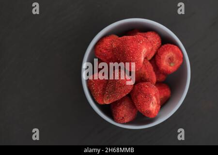 Gefrieren Sie getrocknete Erdbeeren in einer blauen Schüssel auf dem schwarzen Holztisch, flacher Fokus Stockfoto