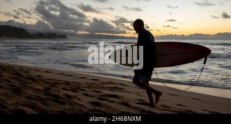 Waikiki, Honolulu, Hawaii - 31. Oktober 2021-bei Sonnenuntergang trägt der Mann ein Surfbrett am Strand. Stockfoto