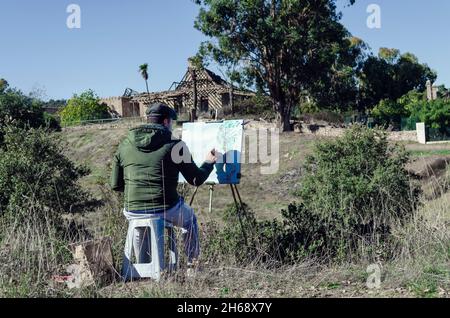 Mann malt eine Landschaft mit einem verlassenen Haus auf dem Land Stockfoto