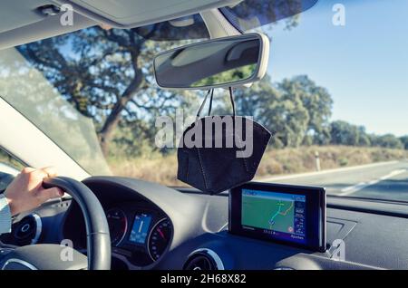 FFP2 Maske, die vom Rückspiegel eines Autos hängt. Selektiver Fokus. Verschwommener Hintergrund. Übersetzung des Wildschweins Stockfoto