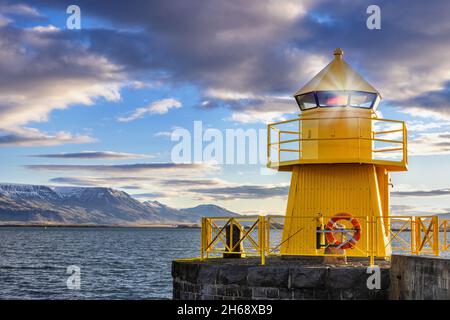 Gelber Leuchtturm im Hafen von Reykjavik bei Sonnenaufgang. Am frühen Morgen mit schneebedeckten Bergen in der Ferne. Island. Stockfoto