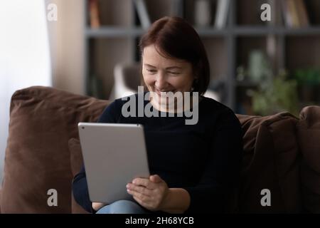 Nahaufnahme lächelnde reife Frau mit Tablet, sitzend auf der Couch Stockfoto