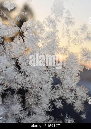 Frostmuster am Fenster mit Blick auf den Sonnenuntergang im Freien hinter Kristalle Stockfoto