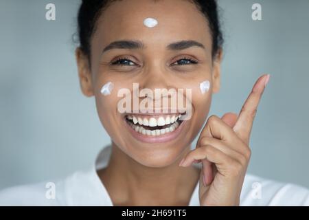 Junge attraktive afroamerikanische Frau, die Creme auf die Wangen auftragen. Stockfoto