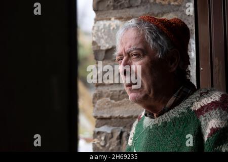 Ein Bergsteiger, älterer erwachsener Mann, Mitte 70, mit handgefertigtem Wollpullover, beobachtet von der Tür einer Berghütte, Pyrenäen, Spanien, aus die Außenseite Stockfoto