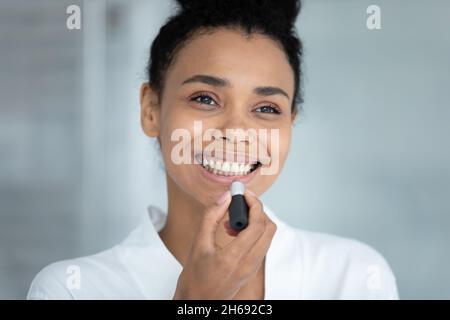 Glückliche junge afrikanische Ethnie Frau Anwendung Lippenstift. Stockfoto