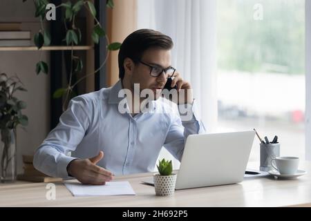 Fokussierter lächelnder junger Geschäftsmann, der im Home Office multitasking. Stockfoto