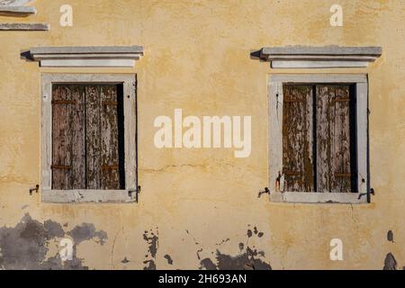 Zwei Fenster in alter Wand mit geschlossenen braunen Fensterläden, Pellestrina Island, venezianische Lagune, Italien Stockfoto