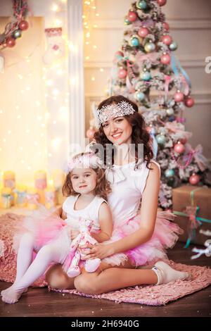 Glamouröse Mutter und Tochter in einem rosa geschwollenen Rock vor dem Hintergrund des Weihnachtsbaums. Stockfoto