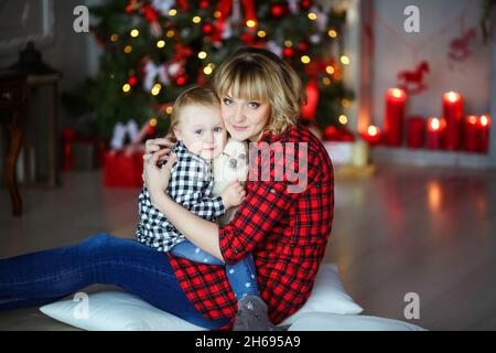 Familie von zwei Personen Mutter und am Silvesterabend in der Nähe des geschmückten Weihnachtsbaums sitzen auf dem Boden mit einem kleinen Haustier. Stockfoto