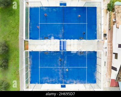 Blick von oben, atemberaubende Luftaufnahme von einigen Menschen, die auf einem blauen Padel-Platz spielen. Padel ist eine Mischung aus Tennis und Squash. Stockfoto