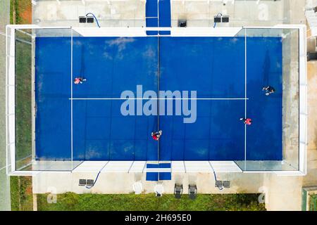 Blick von oben, atemberaubende Luftaufnahme von einigen Menschen, die auf einem blauen Padel-Platz spielen. Stockfoto