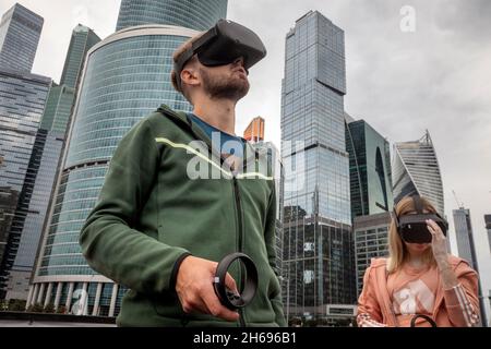 Moskau, Russland. 21. August 2021 EIN junges Paar mit einer Virtual-Reality-Brille wird beim Geek Picnic Science Technology Festival vor dem Hintergrund der Wolkenkratzer des Finanz- und Bürozentrums „Moscow City“ in Moskau, Russland, abgebildet Stockfoto