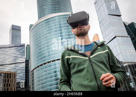 Moskau, Russland. 21. August 2021 Ein junger Mann mit Virtual-Reality-Brille wird beim Geek Picnic Science Technology Festival vor dem Hintergrund der Wolkenkratzer des Finanz- und Bürozentrums „Moscow City“ in Moskau, Russland, abgebildet Stockfoto