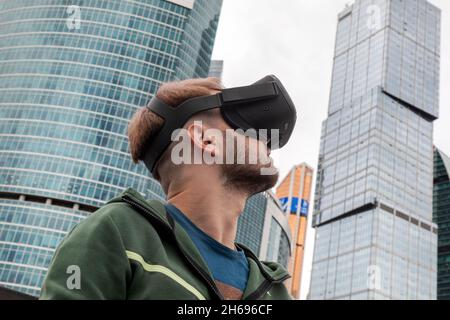 Moskau, Russland. 21. August 2021 Ein junger Mann mit Virtual-Reality-Brille wird beim Geek Picnic Science Technology Festival vor dem Hintergrund der Wolkenkratzer des Finanz- und Bürozentrums „Moscow City“ in Moskau, Russland, abgebildet Stockfoto