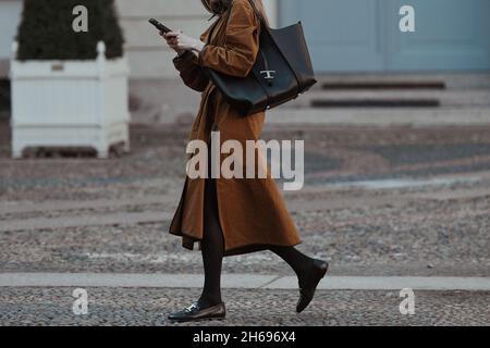 Mailand, Italien - 24. September 2021: Street-Style-Outfit, modische Frau trägt einen Kamel geknöpften langen übergroßen Split-Mantel, ein schwarzes glänzendes Leder b Stockfoto