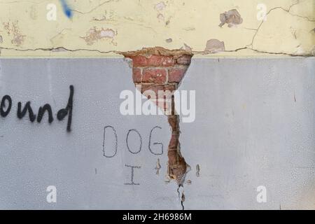 Altes Mauerwerk unter rissigem Putz an einer gelb-grau gestrichenen Wand. Referenzmaterial für Künstler. Stockfoto