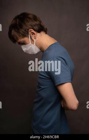 Junger, hübscher, großer, schlanker weißer Mann mit braunen Haaren, gesättelt, trägt eine Gesichtsmaske in blauem Hemd auf grauem Hintergrund Stockfoto