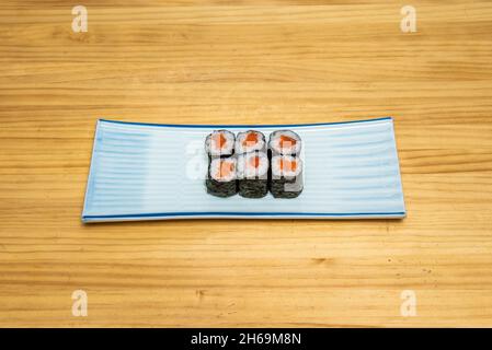 Norwegisches Lachs-Hosomaki-Sushi mit Reis gewürzt mit japanischem Essig in Nori-Algen auf blauem Teller Stockfoto