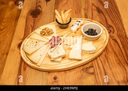 Große Tafel mit verschiedenen Käsesorten, Marmeladen, getrockneten Tomaten, Walnüssen und picos camperos als Tapas oder als Aperitif auf einem Holztisch Stockfoto