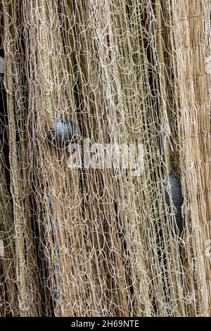 Fischernetze, die an einer Wand hängen, um in der Sonne zu trocknen, Fischernetze, die in der Sonne trocknen, Schleppernetze für die Fischerei, die bereit für den Einsatz auf Booten aufgehängt werden. Stockfoto