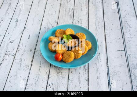 Portion Hühnchen-Nuggets in Mehl und Ei mit Käsesauce zerschlagen, um auf einen blauen Teller zu tauchen Stockfoto