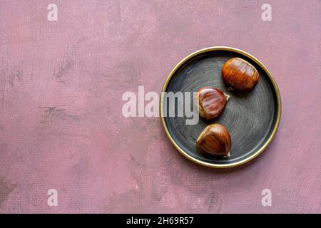 Saftige Kastanien auf einem Vintage-Metallteller auf rosa lackierter Oberfläche Stockfoto