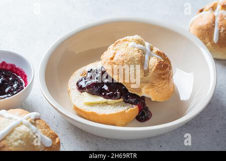 Traditionelle Osterbrötchen mit Rosinen, Butter und Beerenmarmelade auf grauem Hintergrund. Stockfoto