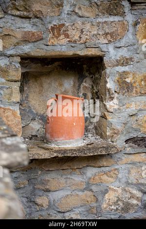 Antiker handgemachter Tonweinkrug mit Spinnennetz, der auf einem Steinfenster in der Mitte der Steinmauer im bulgarischen Dorf steht. Dekoration und Handwerk für b Stockfoto