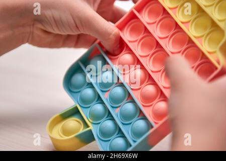 Kinder Hände schieben sensorische Pop it. Farbenfrohe Antistress-Spielzeuge, einfache Grübchen, Pop-Tube. Rainbow Silikon sensorische Fidget Neue beliebte trendige Silikon-Spielzeug. Stockfoto