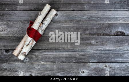 Ansicht von oben auf verzierte weiße Birkenstämme, die in rotes Tuch auf alte Holzplanken gewickelt sind, für einen fröhlichen Weihnachtshintergrund Stockfoto