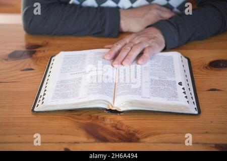 Älterer Mann, der betet und eine alte Bibel liest. Hände gefaltet im Gebet auf einer Heiligen Bibel in der Kirche Konzept für Glauben, Spiritualität und Religion Stockfoto