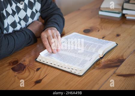 Älterer Mann, der betet und eine alte Bibel liest. Hände gefaltet im Gebet auf einer Heiligen Bibel in der Kirche Konzept für Glauben, Spiritualität und Religion Stockfoto