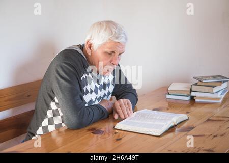 Älterer Mann, der betet und eine alte Bibel liest. Hände gefaltet im Gebet auf einer Heiligen Bibel in der Kirche Konzept für Glauben, Spiritualität und Religion Stockfoto