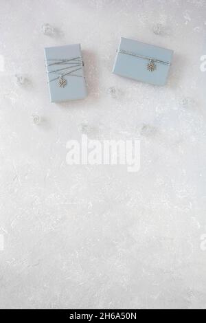 Zwei graue Geschenkschachteln mit silbernem Band und Schneeflocken-Anhänger, auf grauem Hintergrund, Draufsicht, Kopierraum Stockfoto